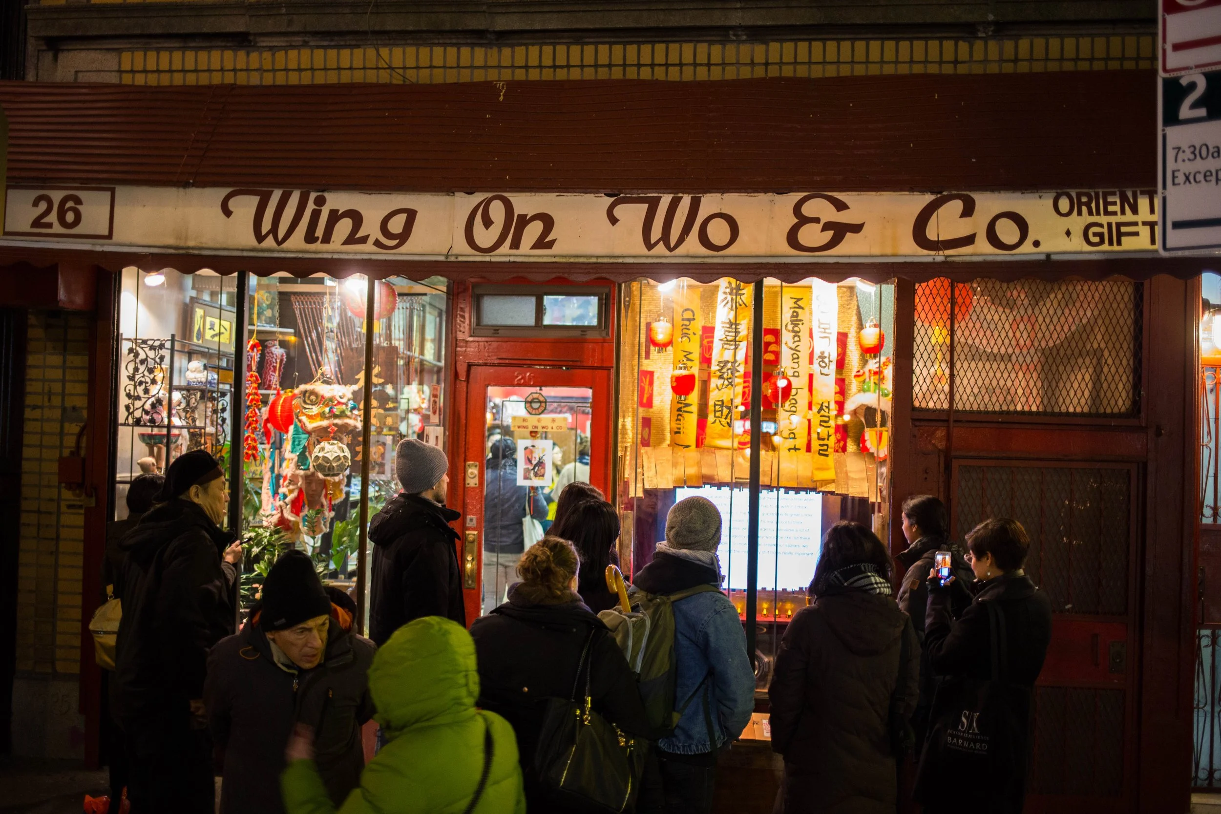 People standing outside a small store called "Wing On Wo & Co" decorated with colorful Chinese lanterns and banners, with a crowd of shoppers inside and outside the store at night.