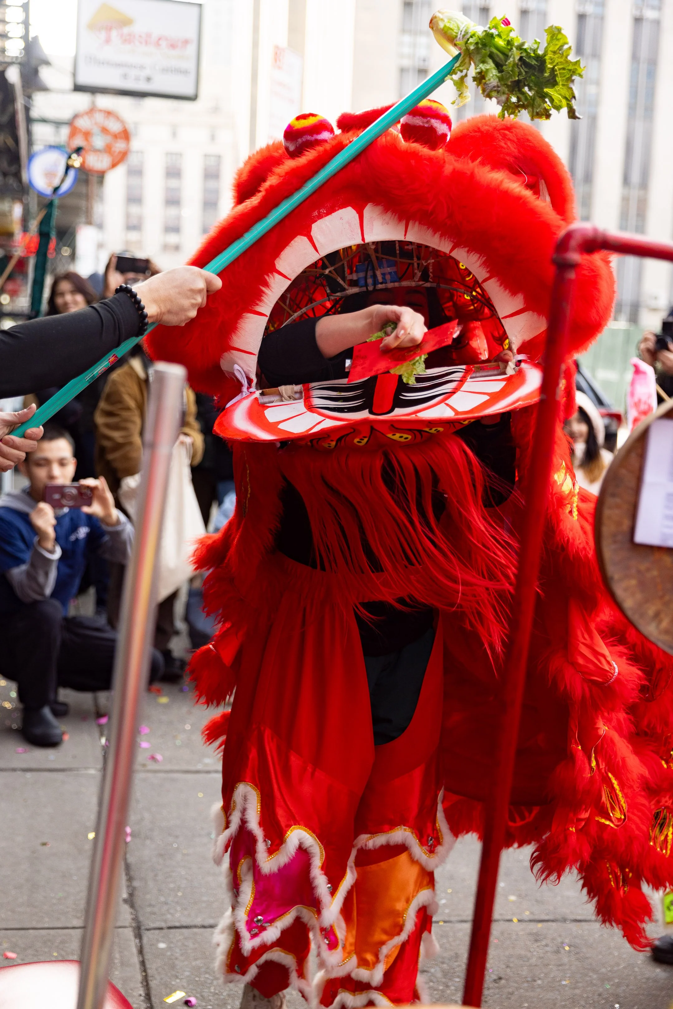 Person in a red traditional lion dance costume performing on a city street with spectators watching.