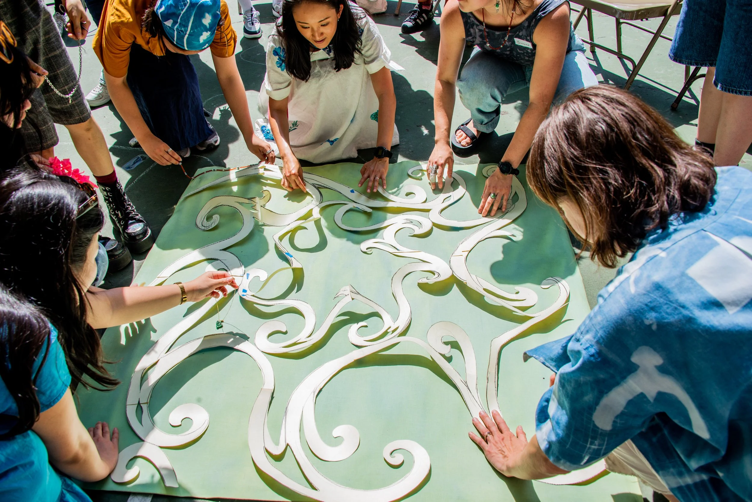 A group of people gathered around a large green board, working together to assemble a puzzle with intricate swirling patterns.