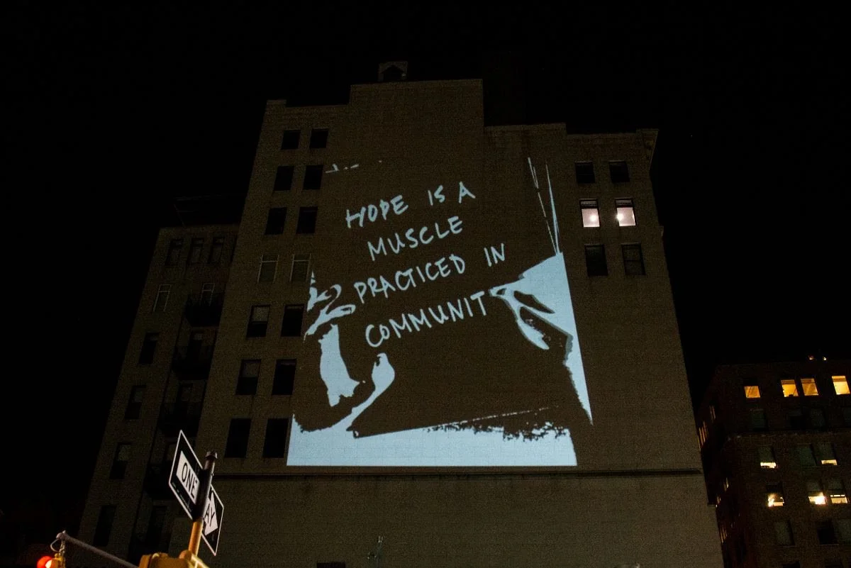 Nighttime projection on building reads, "Hope is a muscle practiced in community."