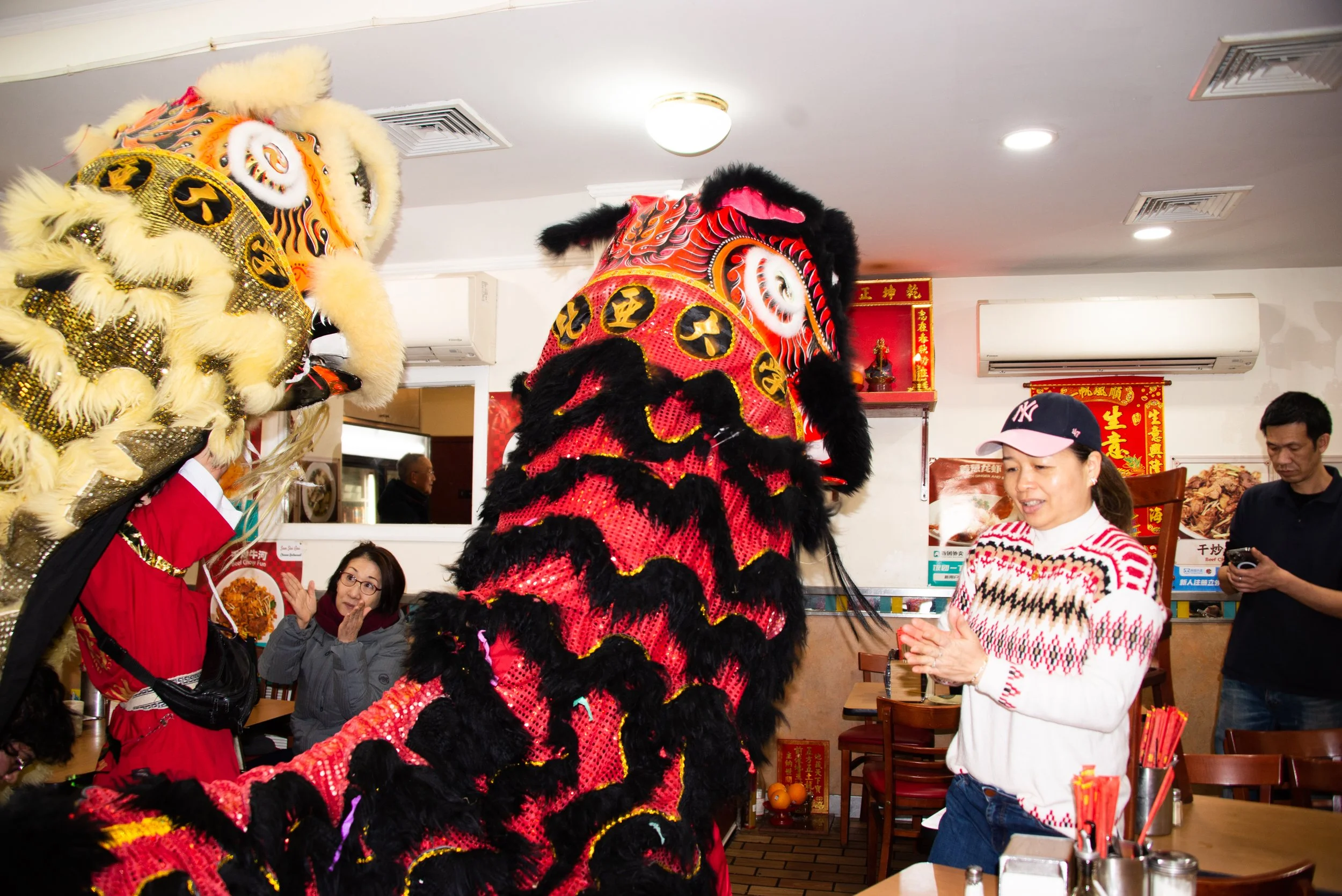 Lion dancers performing inside a restaurant during a festive celebration with onlookers and decorations.