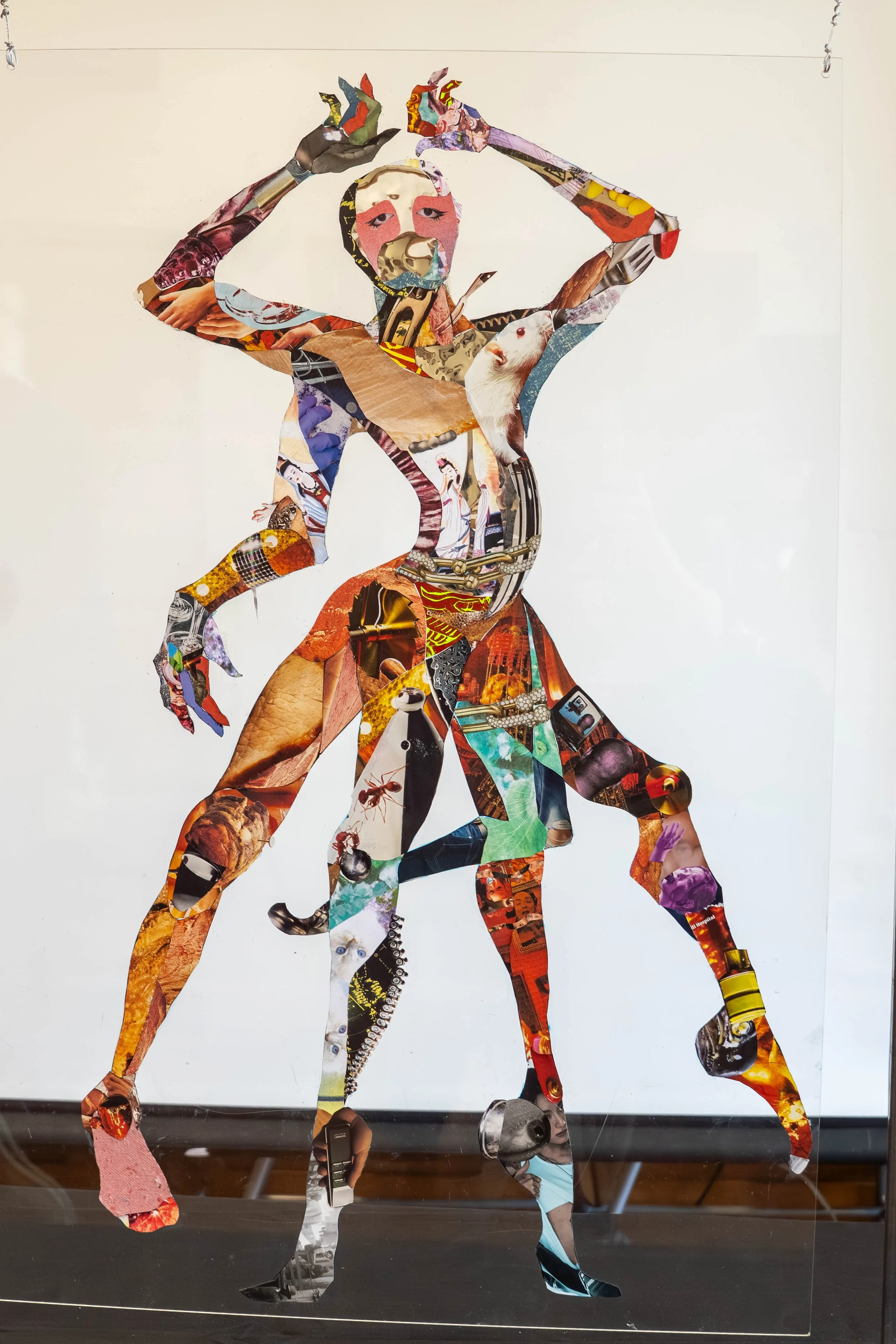 Collage artwork featuring multiple layered cutouts of various images forming a figure with arms raised above head, set against a plain background.