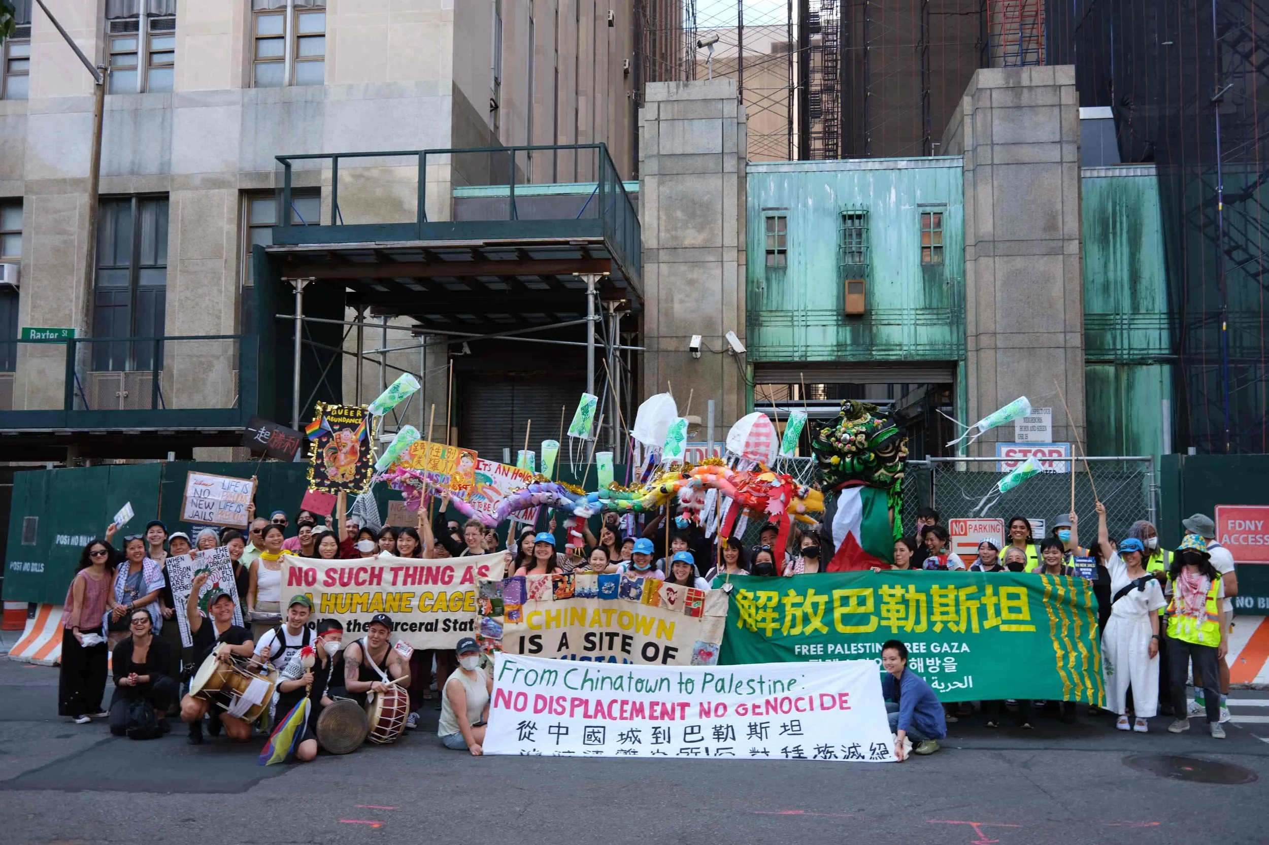 A large group of people protesting on a city street, holding signs and banners supporting Palestine and opposing displacement and genocide, with some people playing drums and wearing masks or hats.