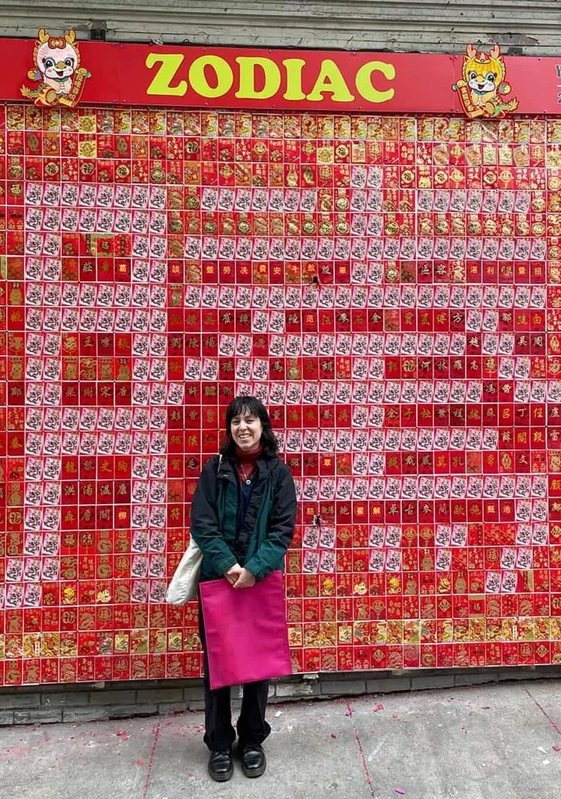 A person standing in front of a large red and gold zodiac sign display with Chinese characters and images, with cartoon lion illustrations at the top corners and a prominent yellow 'ZODIAC' sign above.
