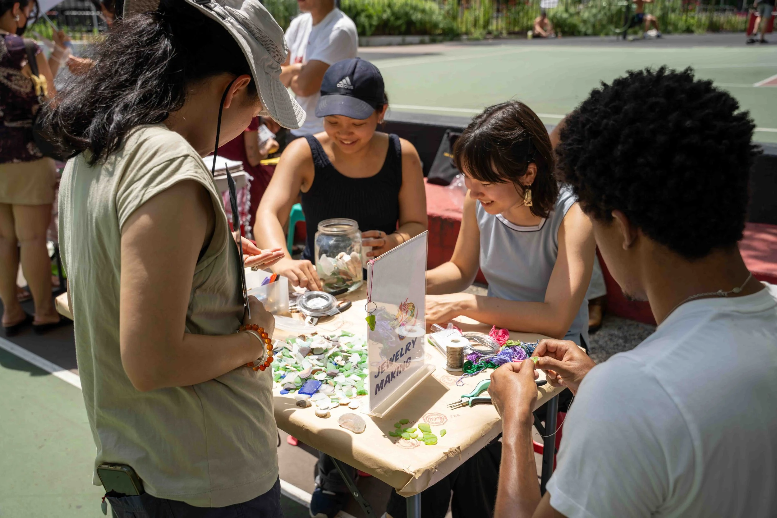Group of people making jewelry at an outdoor craft table.