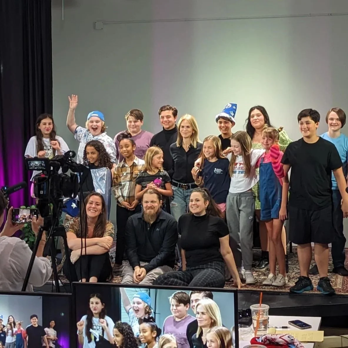 Group of people posing for a photo on a set, with a camera visible in the foreground.
