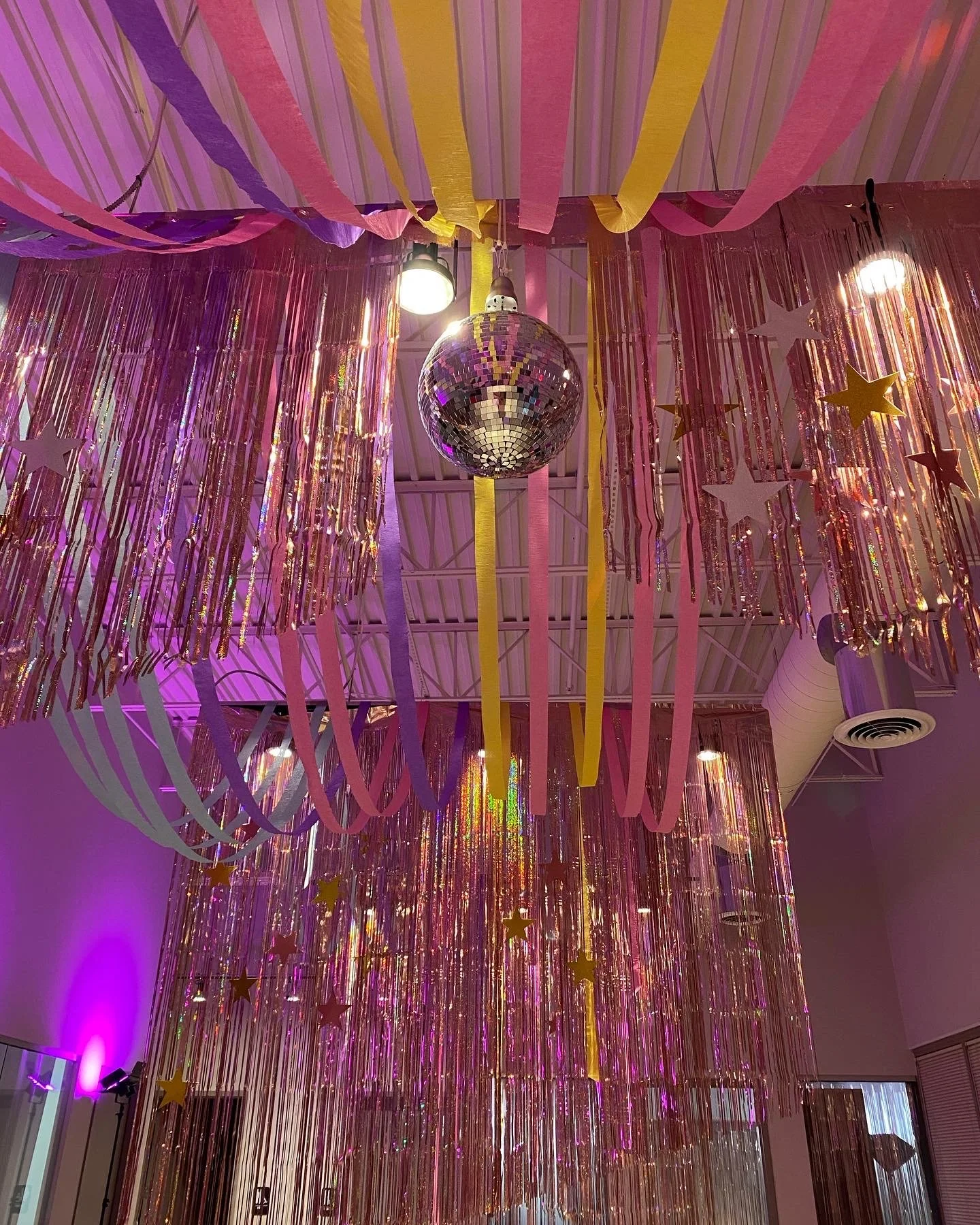 Ceiling decorated with pink, yellow, and purple streamers, a hanging disco ball, and star-shaped decorations.