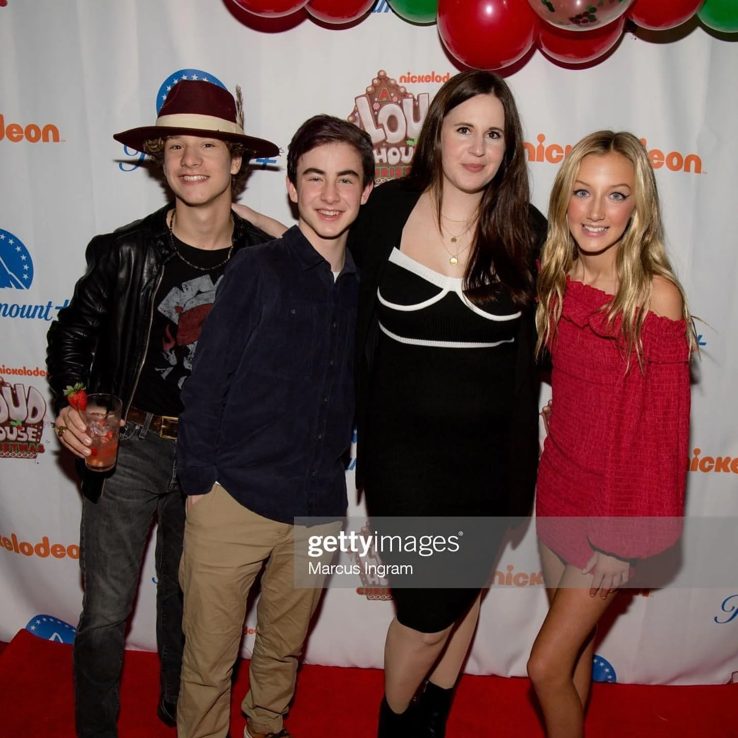 Group of four people posing at a Nickelodeon event on a red carpet with a Nickelodeon and Paramount Plus backdrop, along with festive balloons.