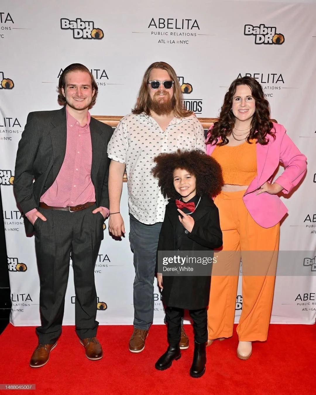 Group of four people posing on a red carpet with a backdrop displaying 'Baby DrO' and 'Abelita Public Relations' logos.