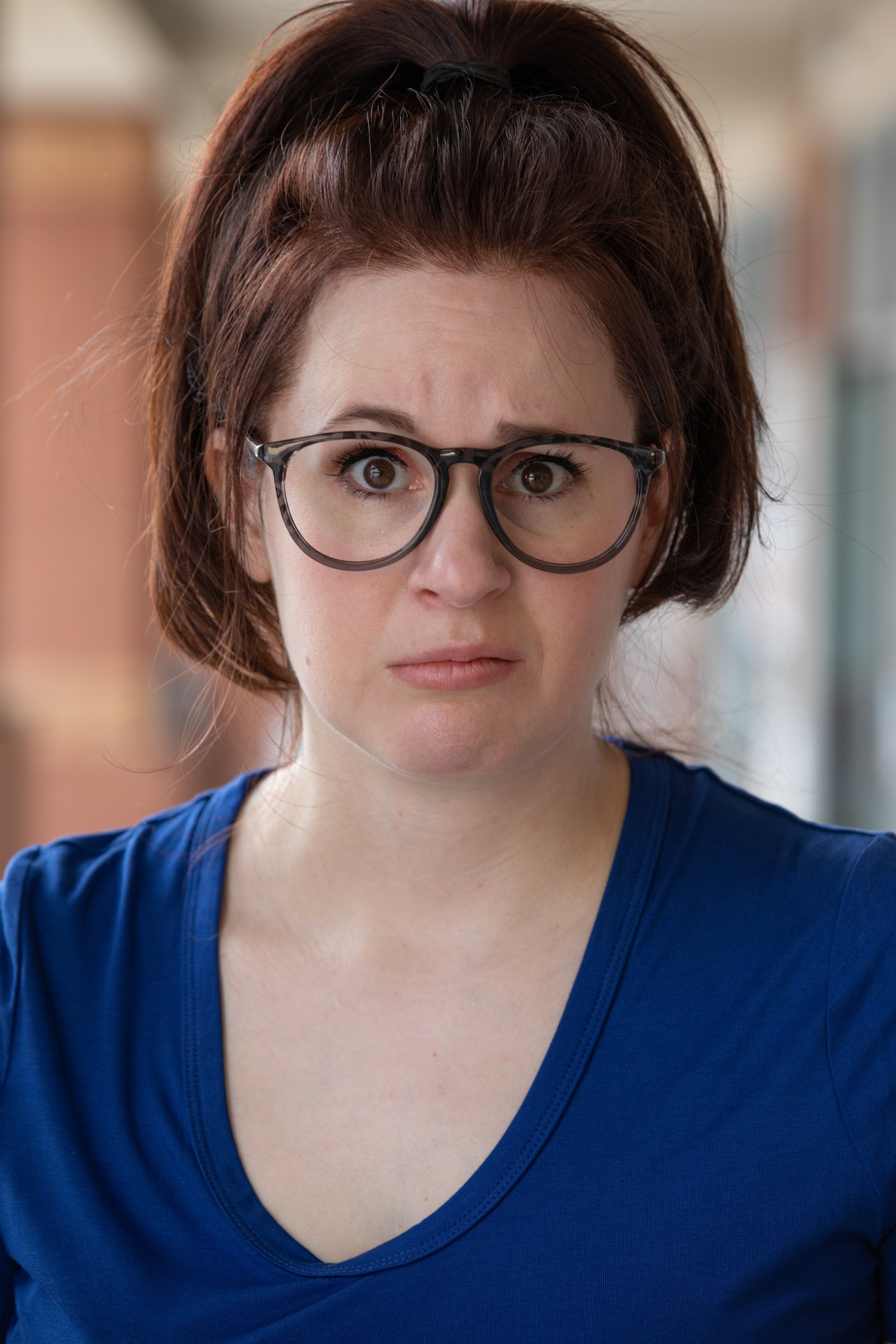 Headshot of actor with glasses looking surprised or confused, wearing a blue shirt.