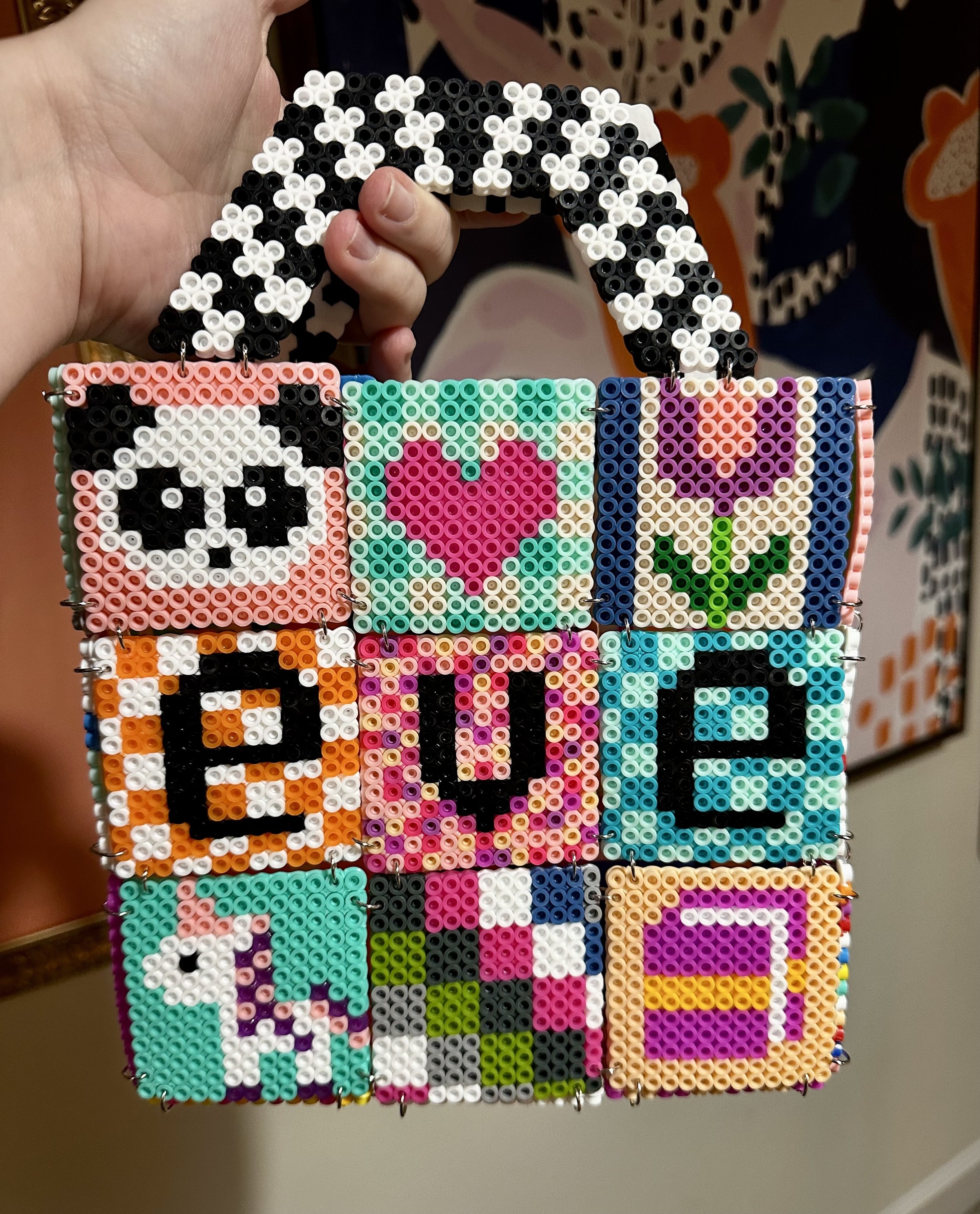 A colorful handbag made of small beads featuring patterns including a panda face, heart, flower, and a unicorn.