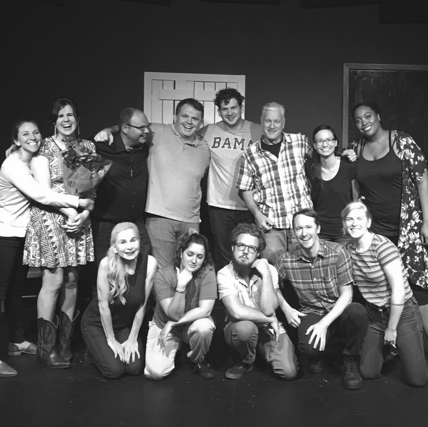 Group of people standing and kneeling on stage, smiling for a photo in black and white.