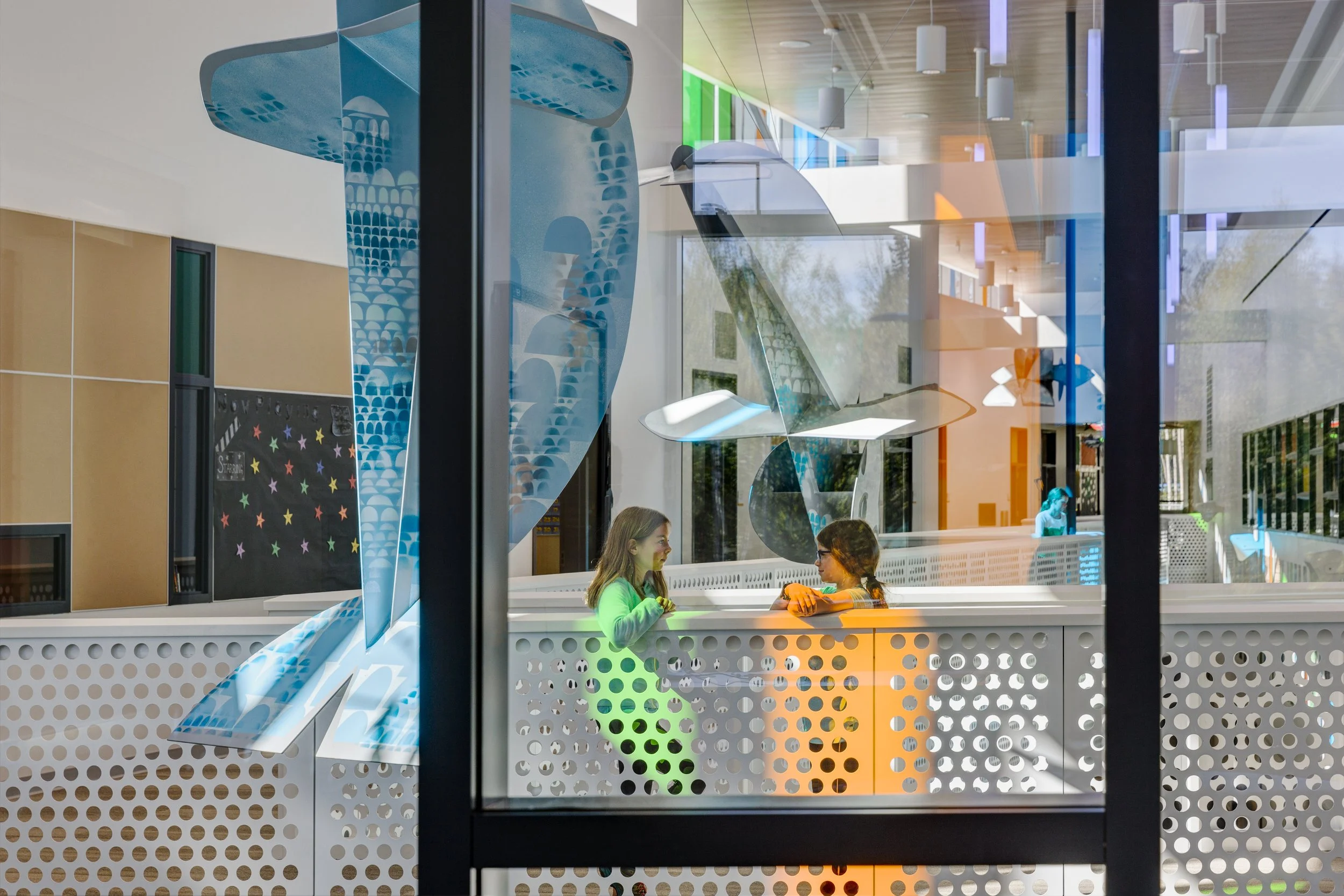 Two people talking in a colorful, modern interior with artistic whale decorations and perforated metal panels.