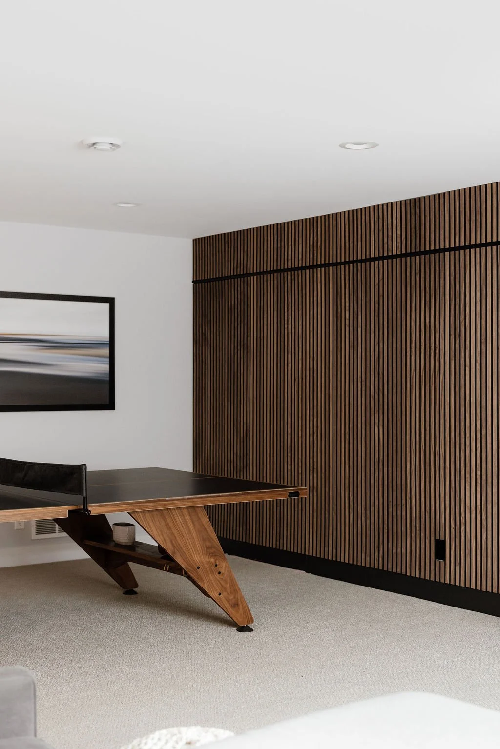 Walnut slat wall, ping pong table and wall art. Black horizontal line in the slat wall making two sections of slat wall. 