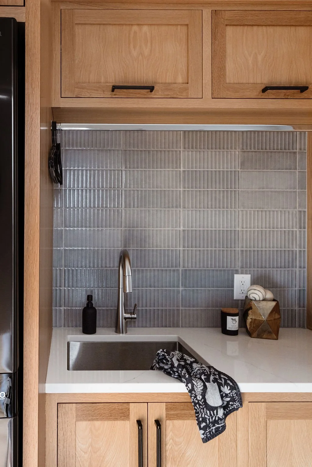 Small modern laundry room with Rift white oak cabinetry, deep utility sink, white quartz countertop, black and stainless accents, clothes hanging rod above the sink.