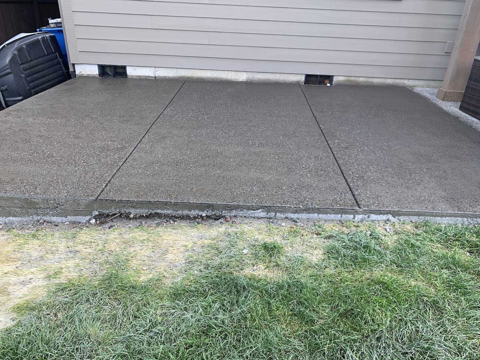 Newly poured concrete patio next to a house with grass in the foreground.