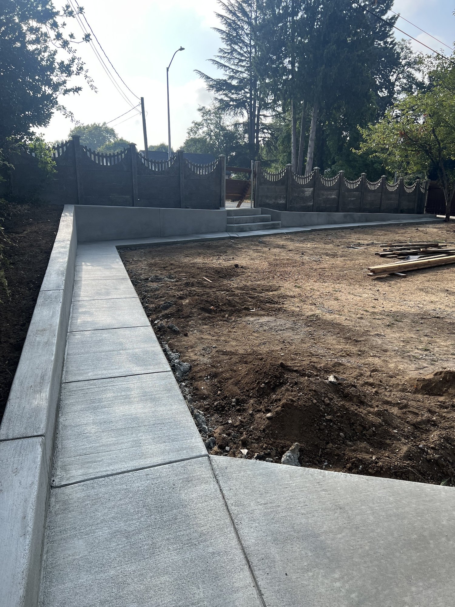 Concrete walkway under construction with surrounding dirt area and a decorative metal fence