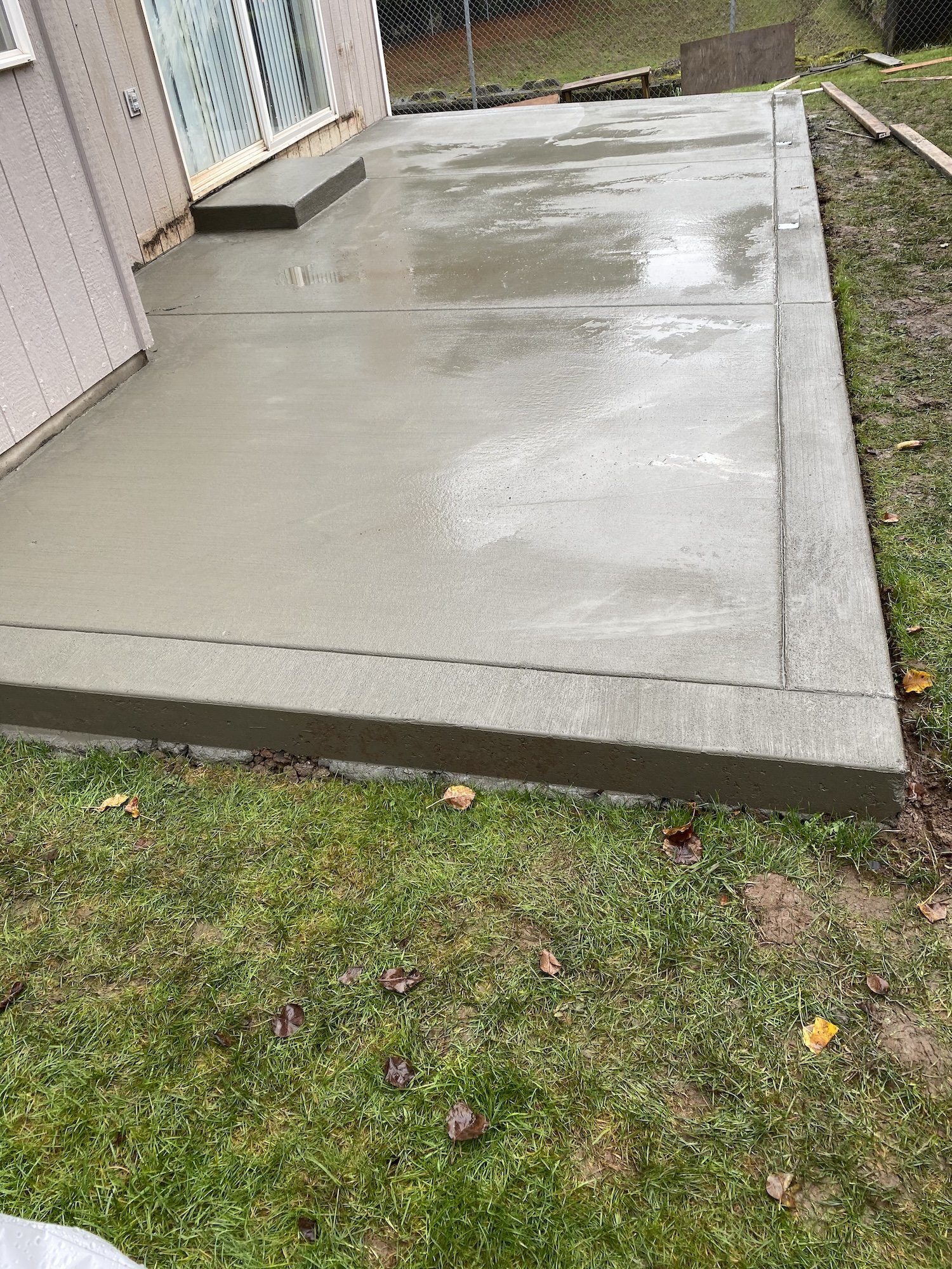 Newly poured concrete patio adjacent to a house with grass surrounding it.