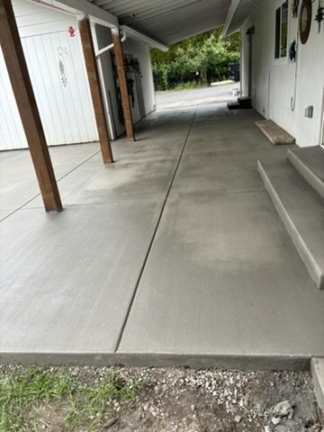 Freshly poured and smoothed concrete patio under a white awning with wooden posts and adjacent white house wall.