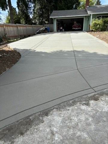 Freshly poured concrete driveway leading to a garage. The clean, smooth surface of the driveway is visible, with surrounding residential landscaping.