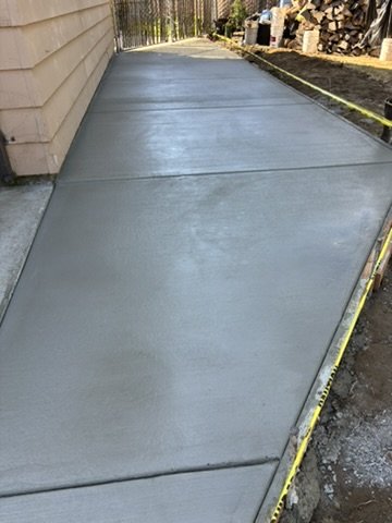 Newly poured concrete sidewalk beside a building, with caution tape along the edge.