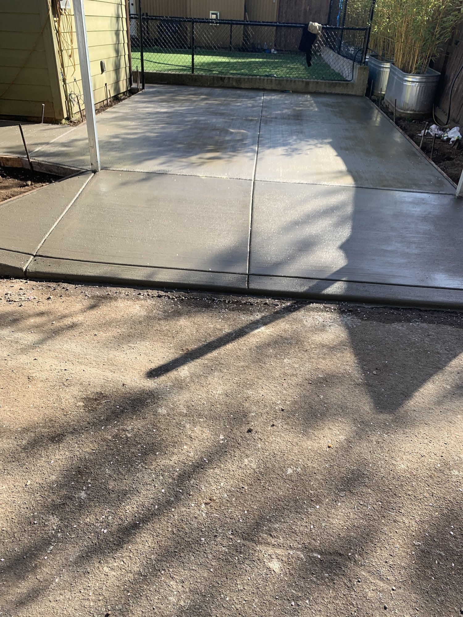 Freshly poured concrete driveway with adjacent lawn and fence