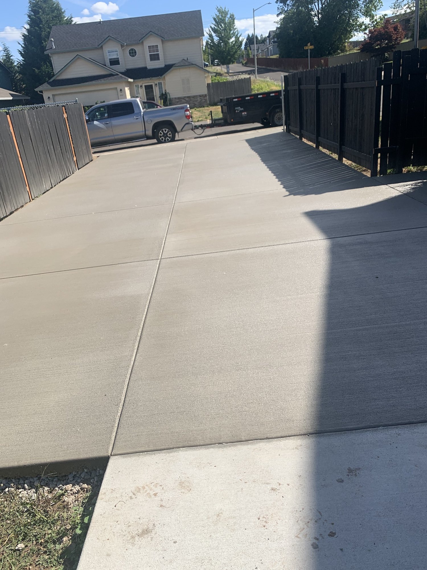 Concrete driveway with shadow, wooden fence, truck, and trailer in suburban neighborhood.