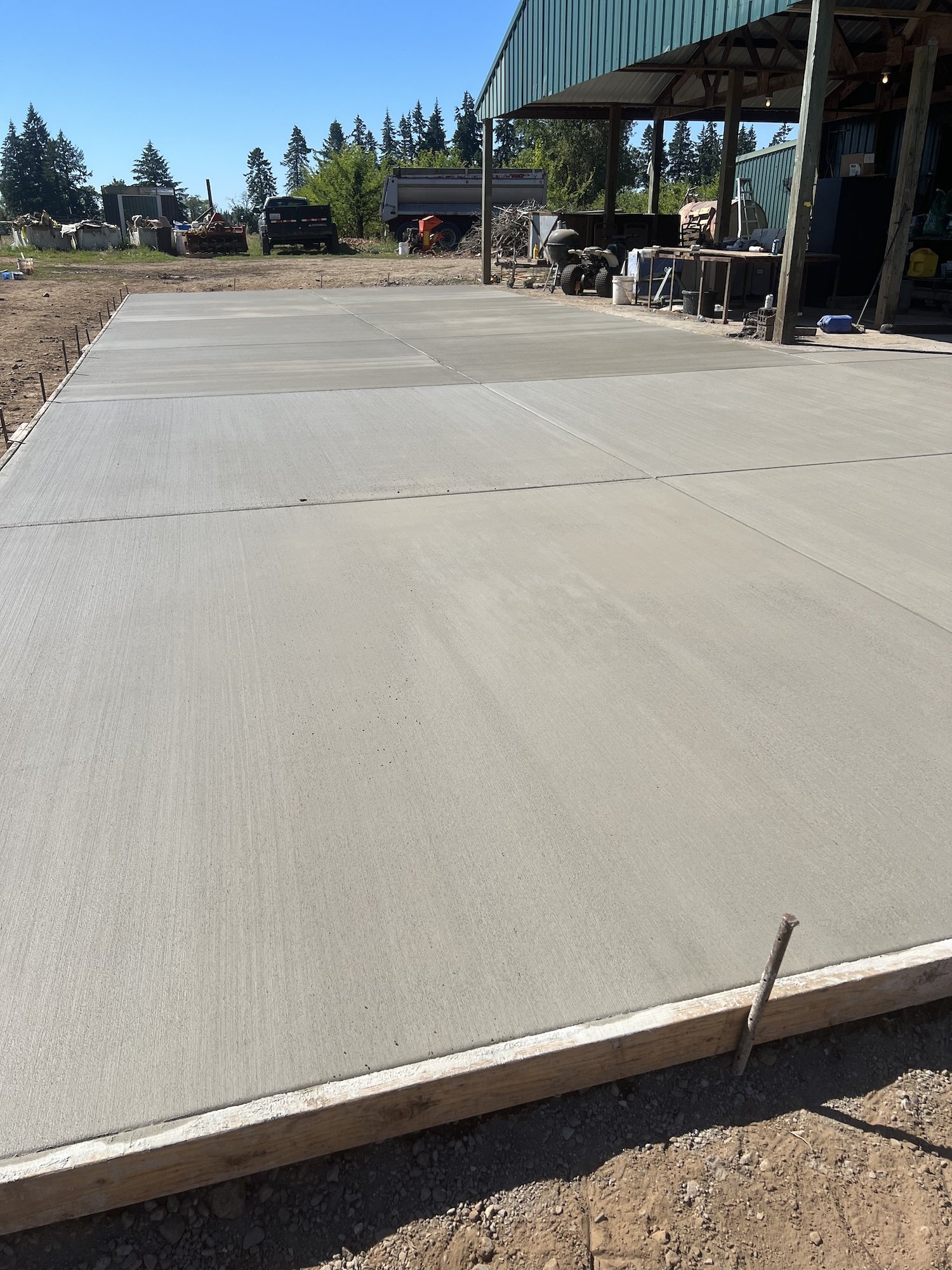 Freshly poured concrete slab drying outdoors with adjacent workshop area.