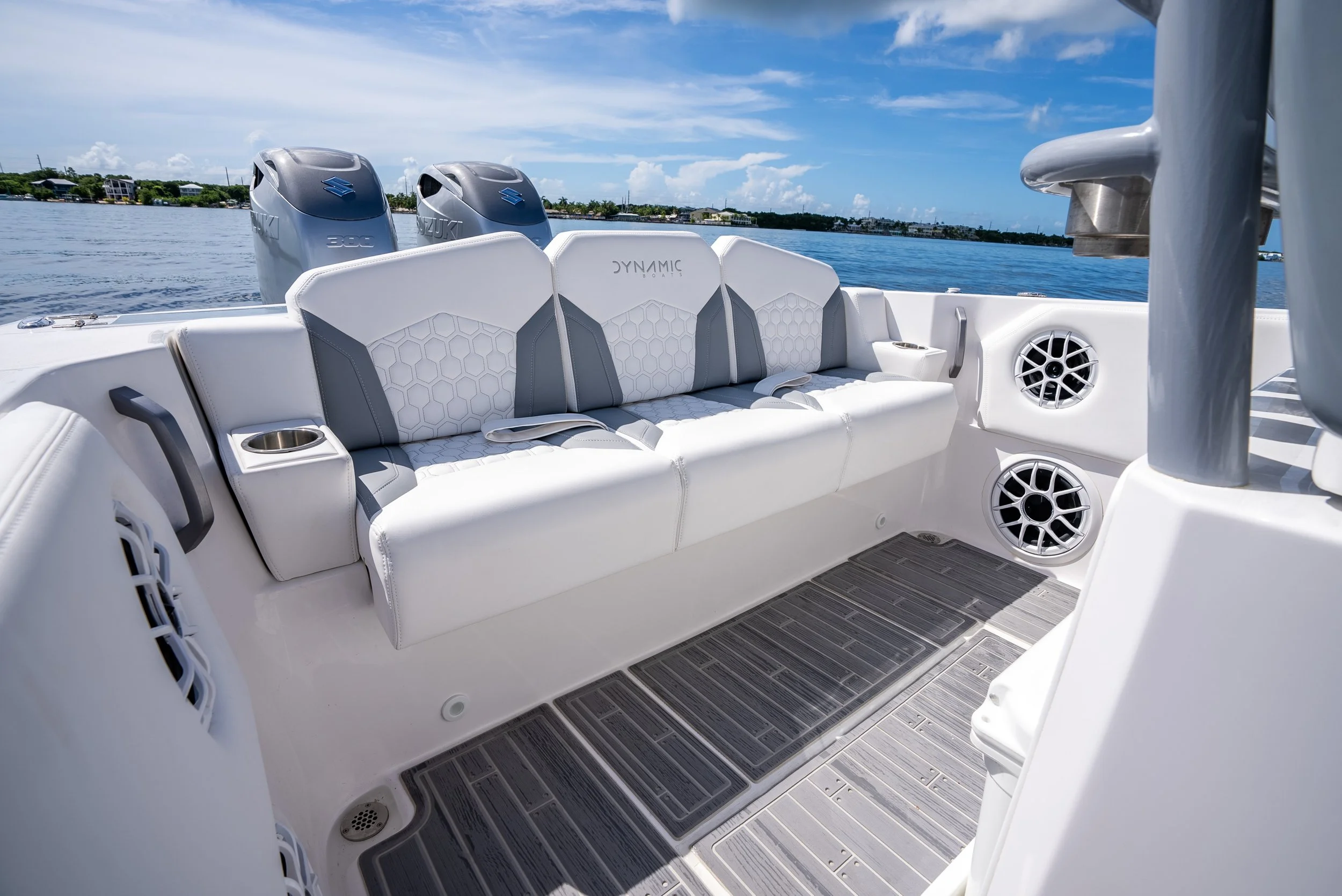 White boat seat with built-in cup holders and two speakers, on a boat with water and a partly cloudy sky in the background.