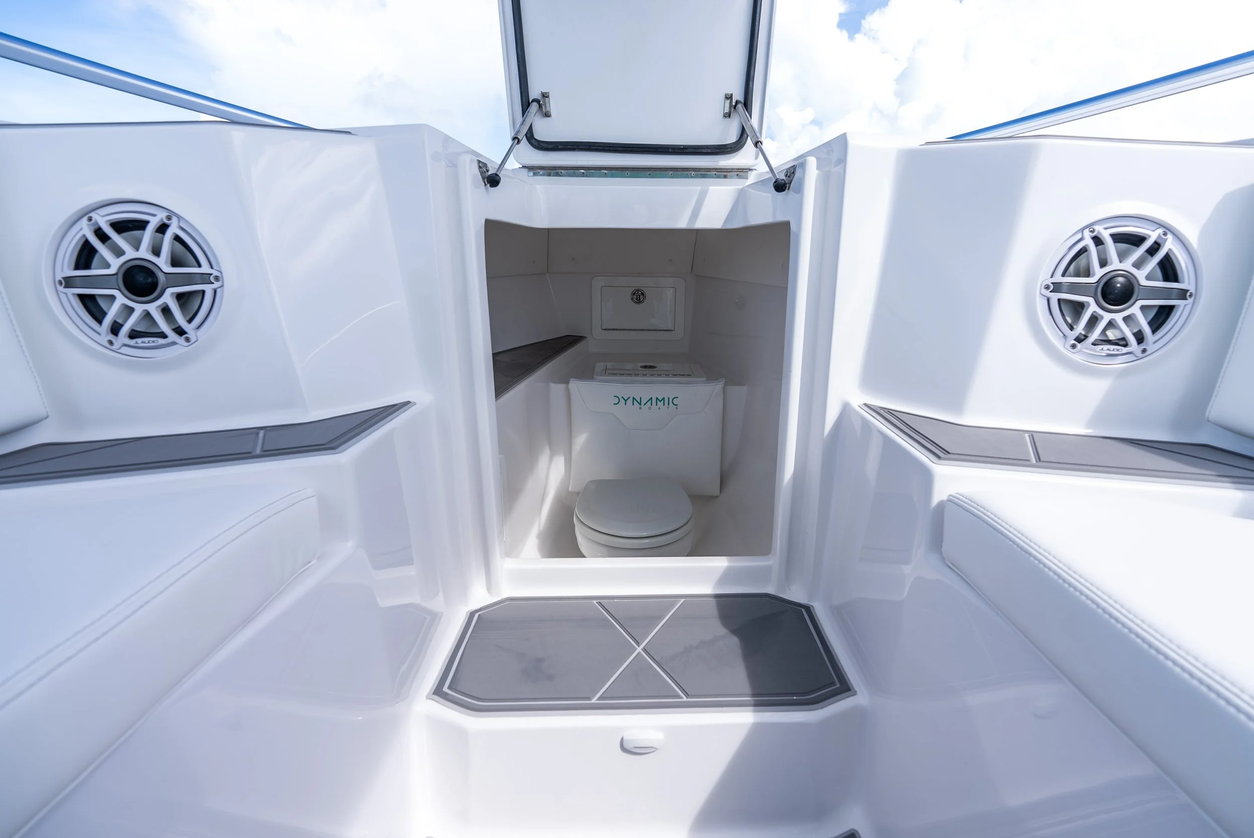 Interior of a boat cabin with a toilet, seating area, and speakers, with a hatch open to the outside sky.