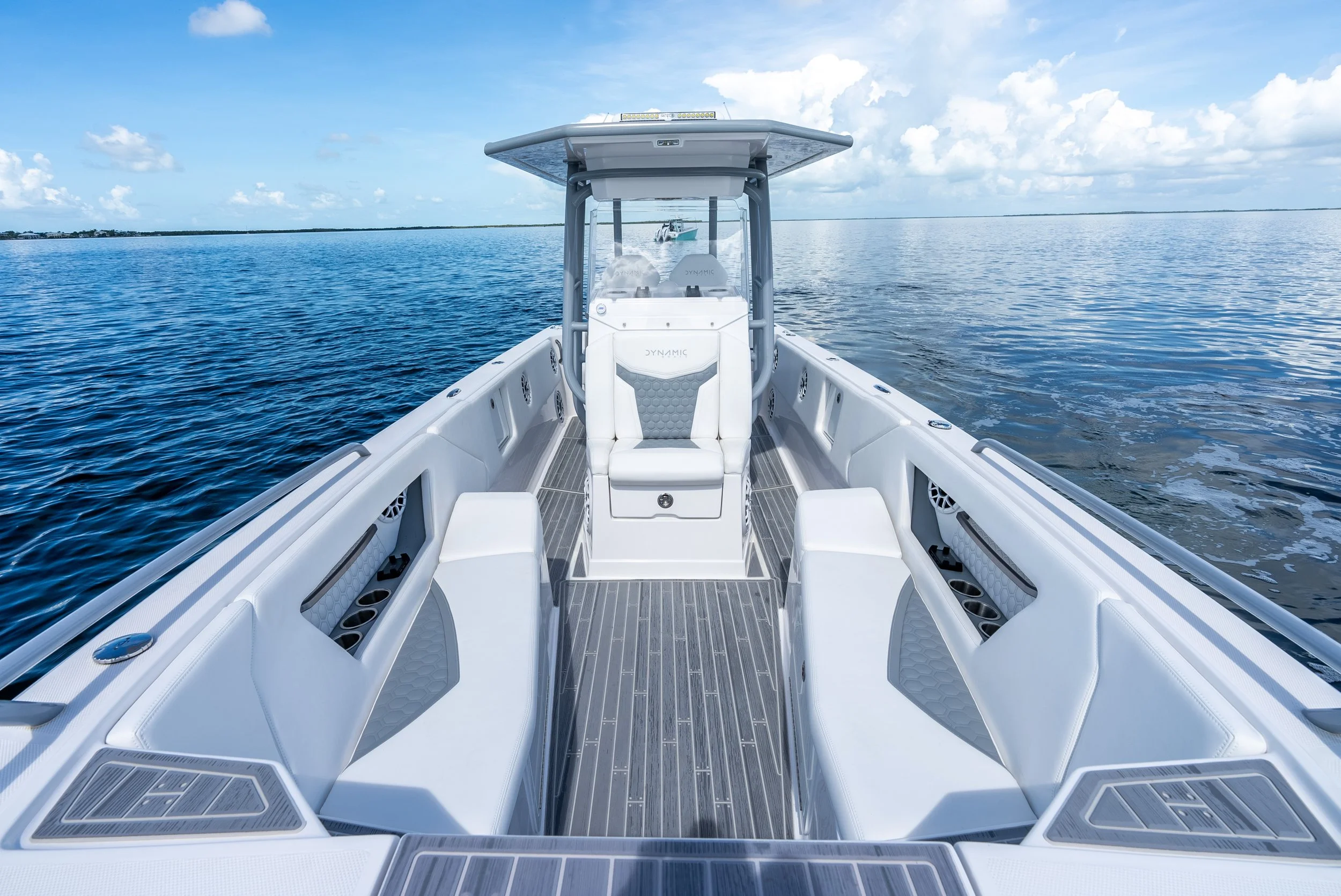 View of a white powerboat on calm blue water under a partly cloudy sky, with land visible in the distance.