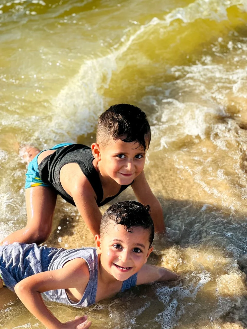 Two young boys playing in shallow ocean water, smiling and enjoying the waves.