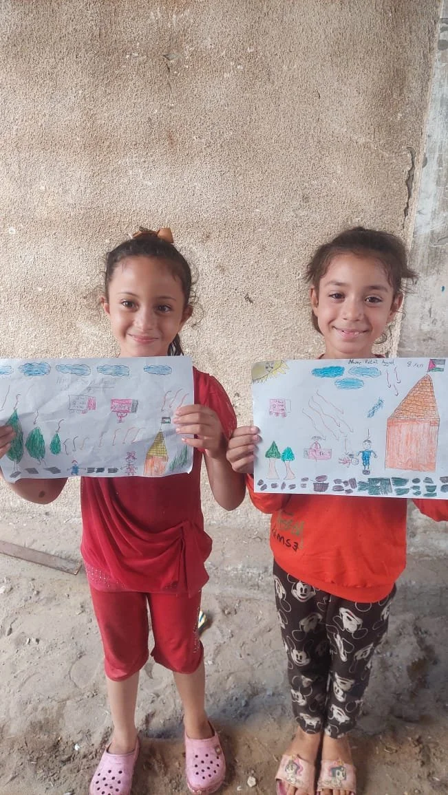 Two girls holding colorful drawings, standing in a casual setting.