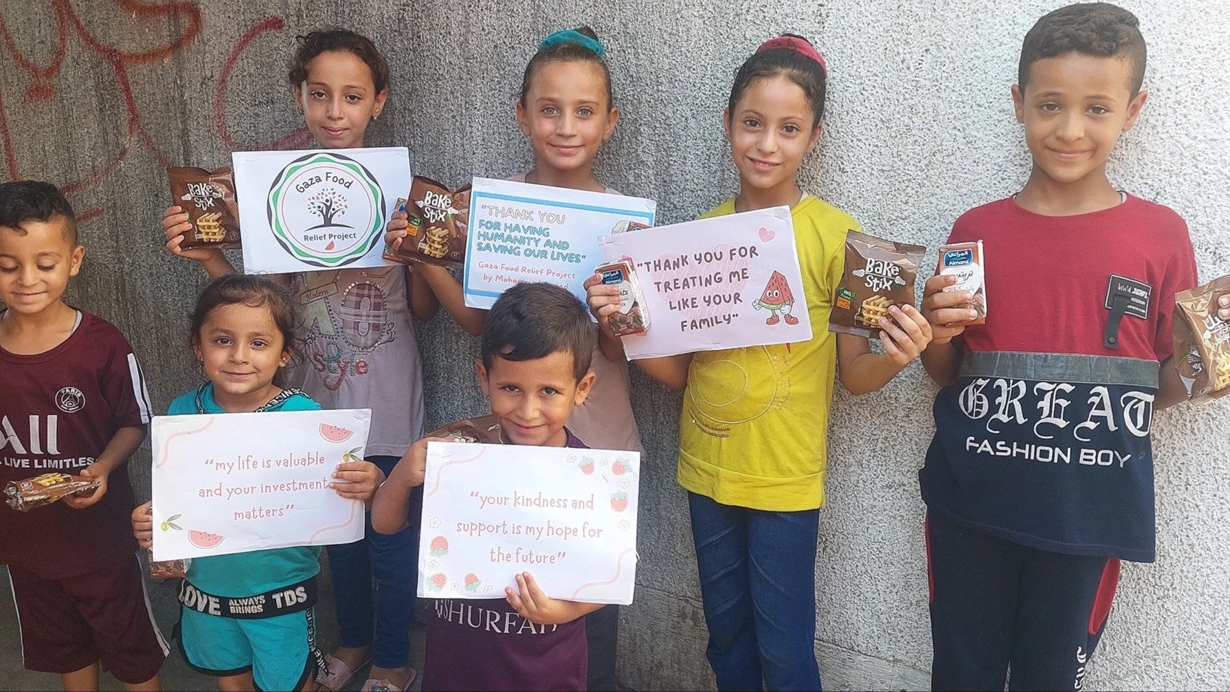 Children holding signs for the Gaza Food Relief Project, expressing gratitude with messages like 'Thank you for treating me like your family' and 'Your kindness and support is my hope for the future.' They are holding snacks and drinks.