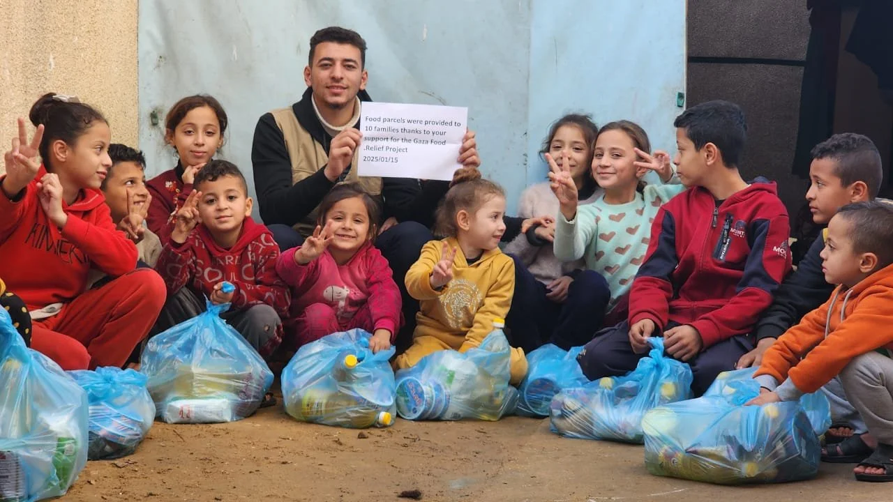 A group of children and an adult with food parcels in blue bags, holding a sign about the Gaza Food Relief Project, dated 2025/01/15.