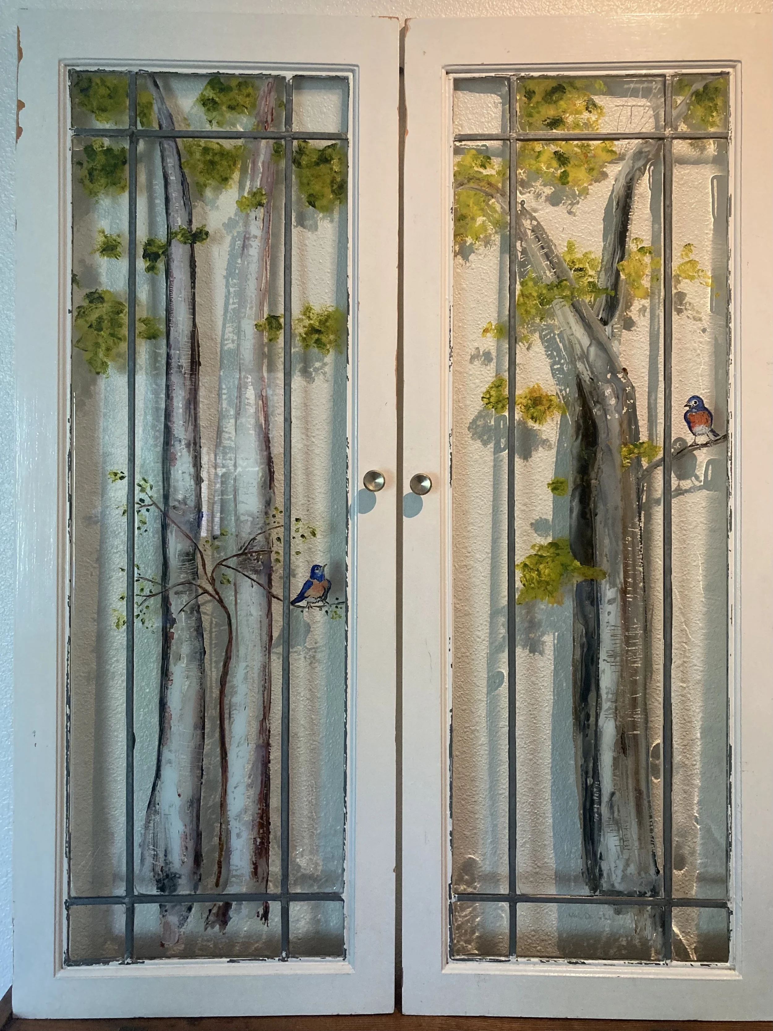 Vintage lead paned glass cabinet doors with handprinted trees, each featuring a bluebird