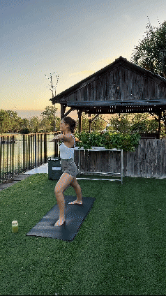 Lilly Moyes practicing yoga outdoors on a mat, performing a warrior pose at sunset. A rustic wooden structure and garden are in the background.
