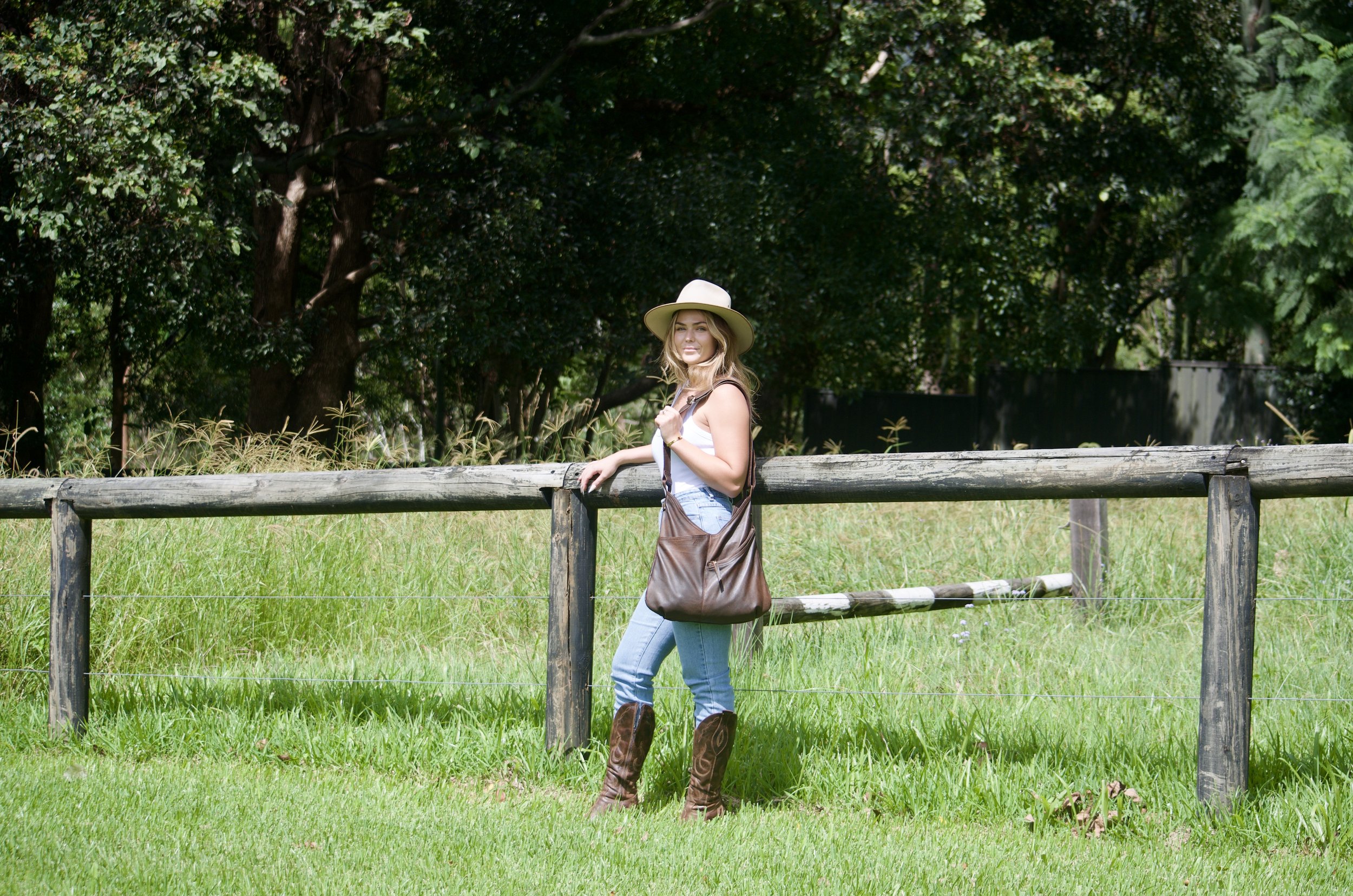 Lilly Moyes in a hat standing by a wooden fence in a grassy field