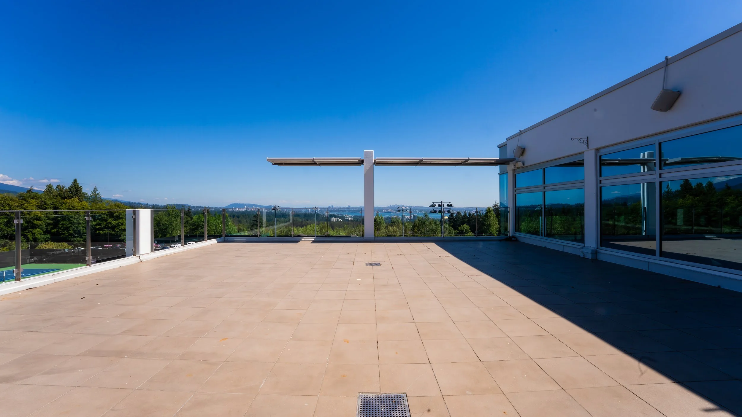 Empty rooftop terrace overlooking cityscape with clear blue sky and glass railing