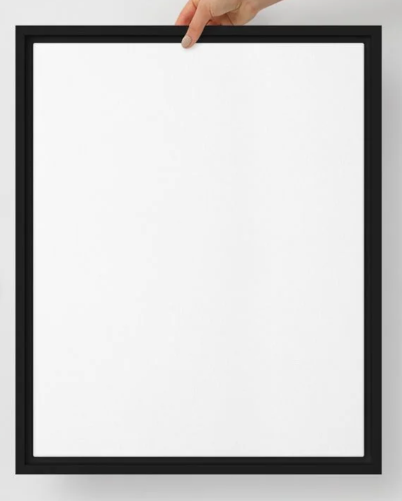 A black-framed blank white canvas held by a person's hand at the top against a white background.
