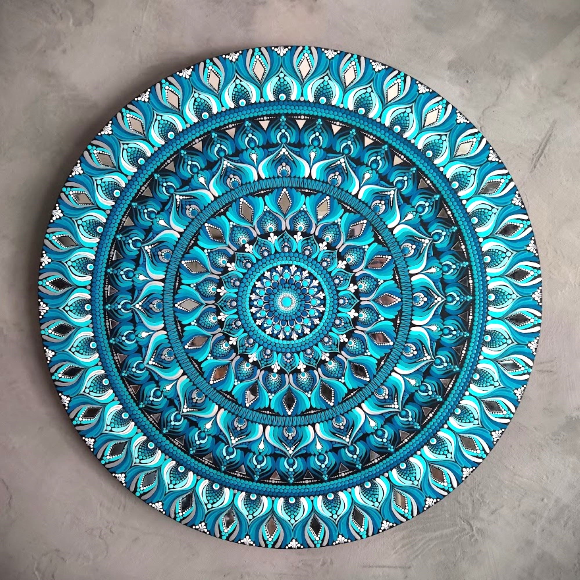 Colorful mandala art with intricate patterns in shades of blue on a textured background.