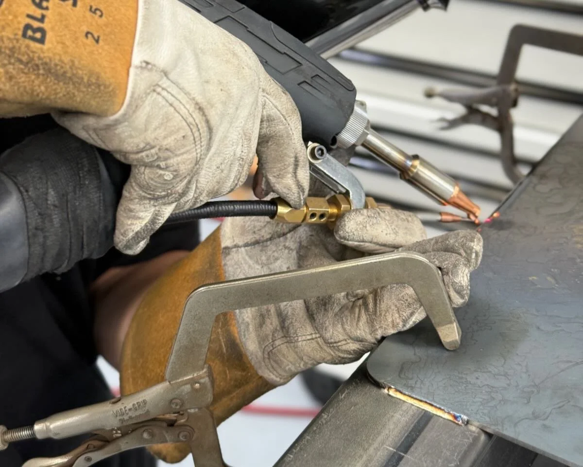 Close-up of a gloved operator laser welding a clamped metal assembly.