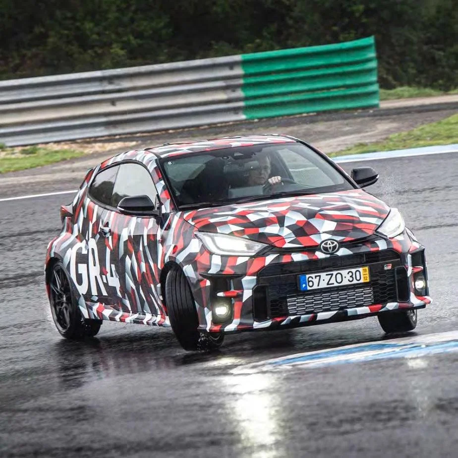 Camouflaged Toyota GR prototype vehicle being driven on a wet test track.