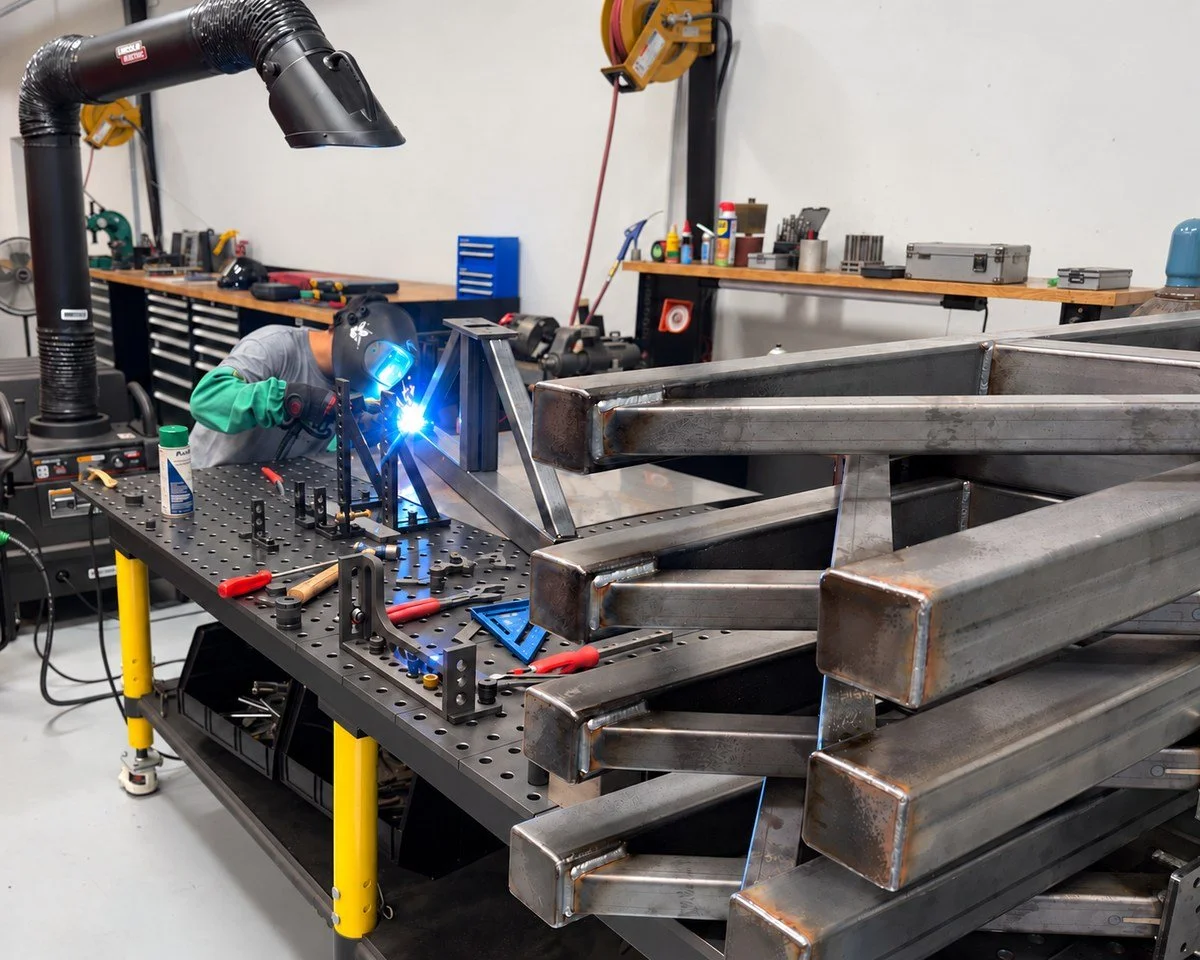 Papadakis Engineering team member welding a steel frame on a fixture table in the fabrication shop.