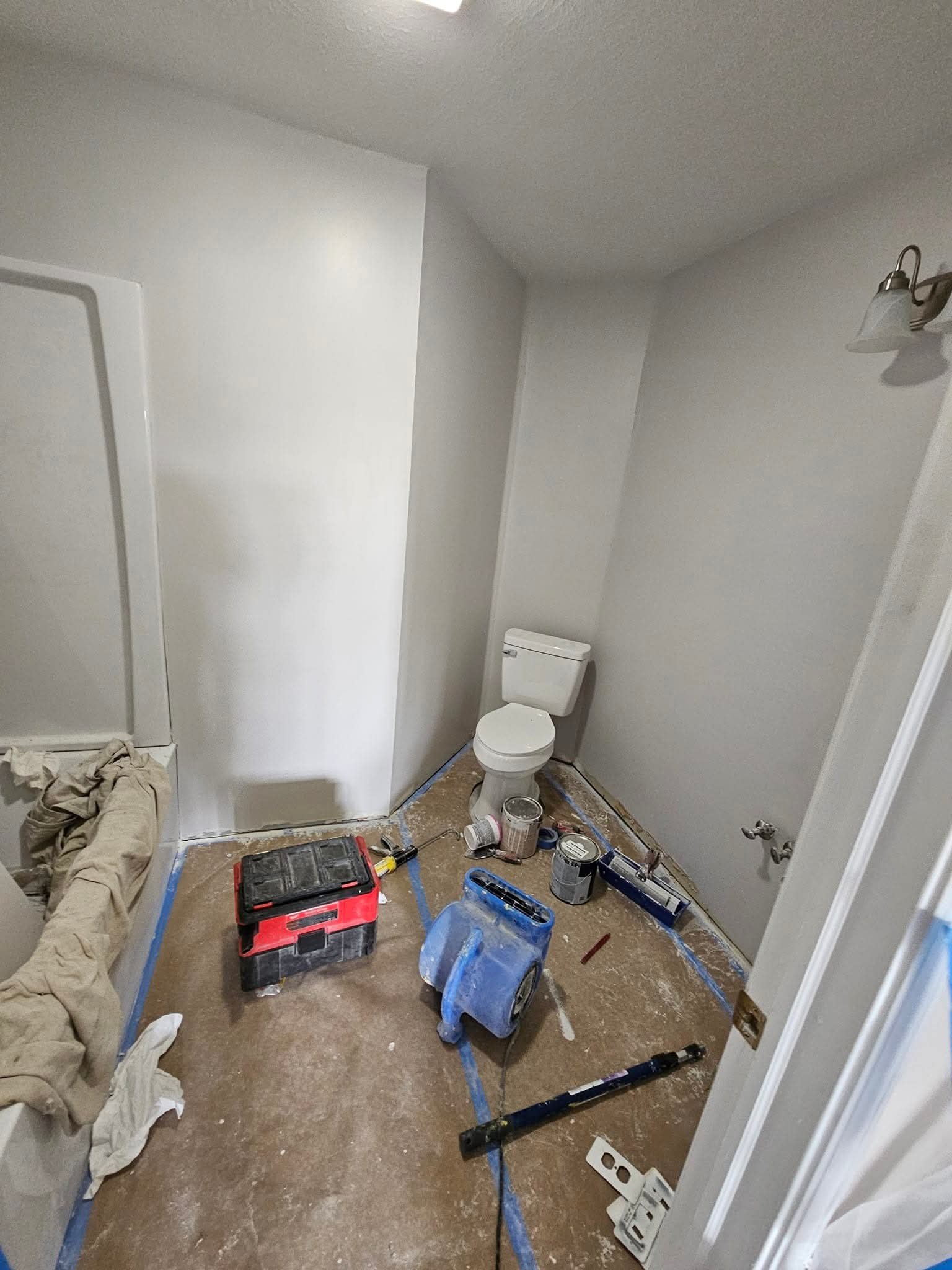 A bathroom under renovation with a toilet, construction tools, paint cans, and supplies scattered across the floor.
