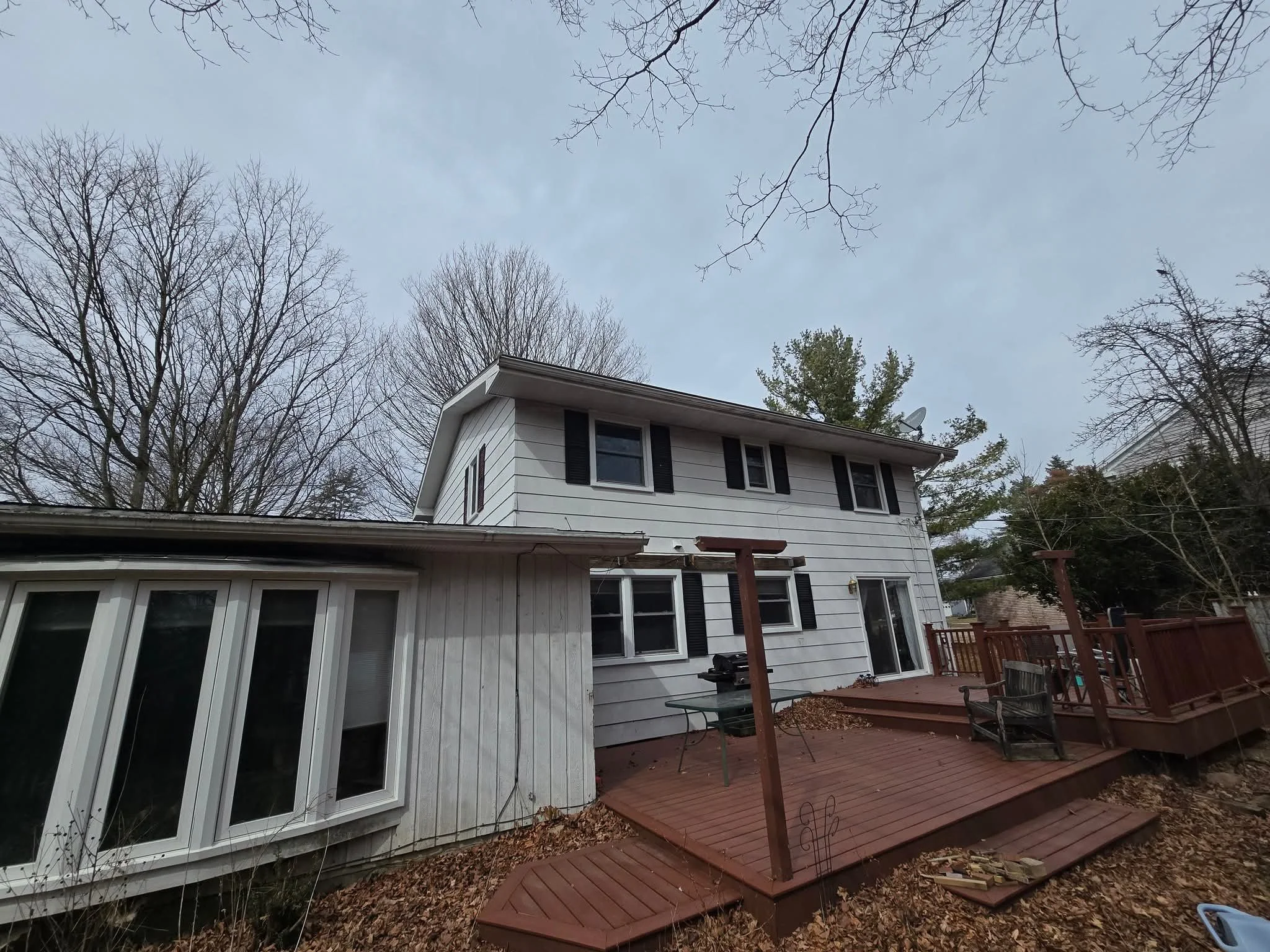 Rear view of a two-story house with a new composite deck, before new vinyl siding