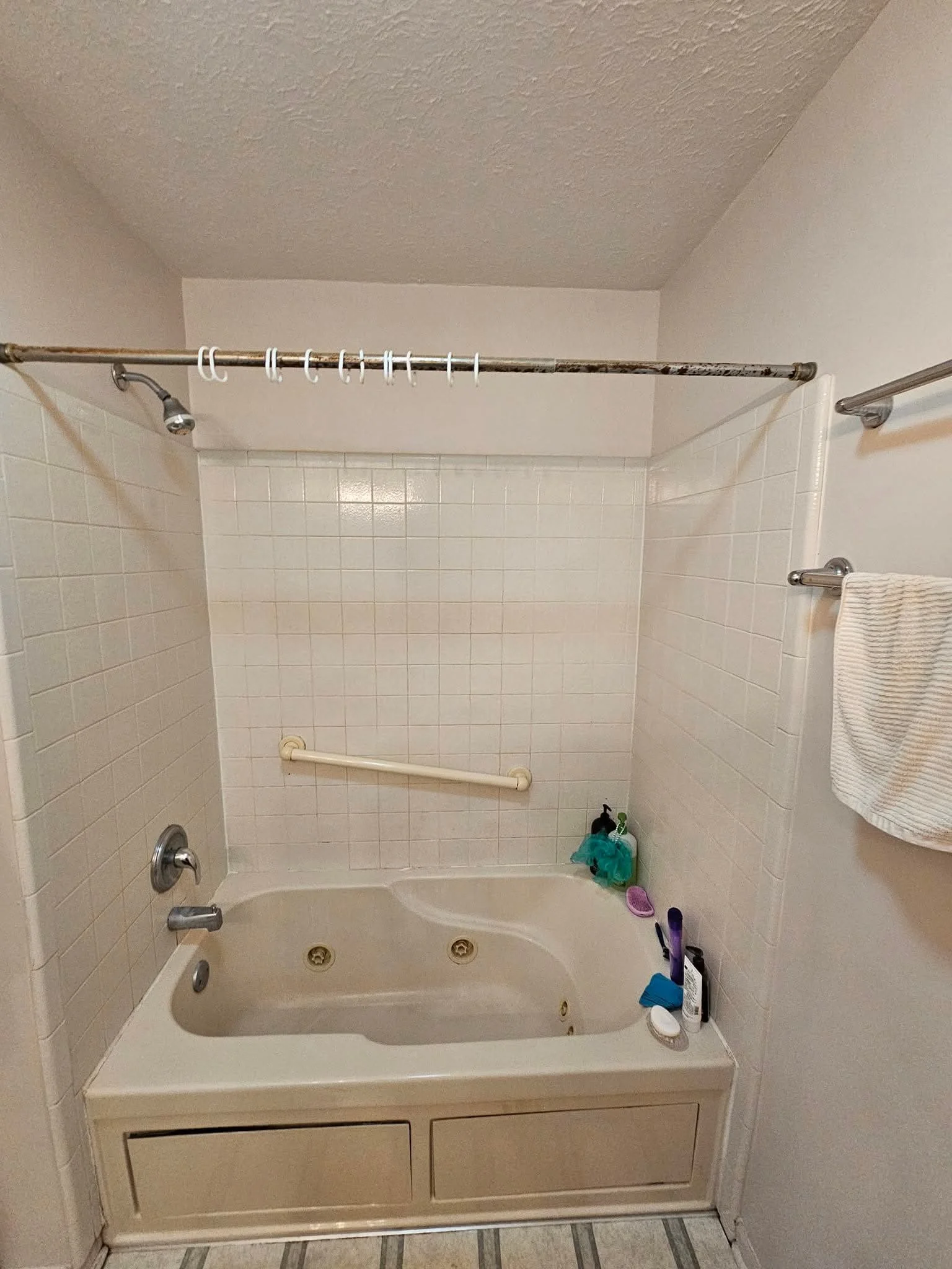 A bathroom with a bathtub, tiled walls, a towel rack with a towel, and a shower curtain rod with hooks. The tub has various toiletries inside.
