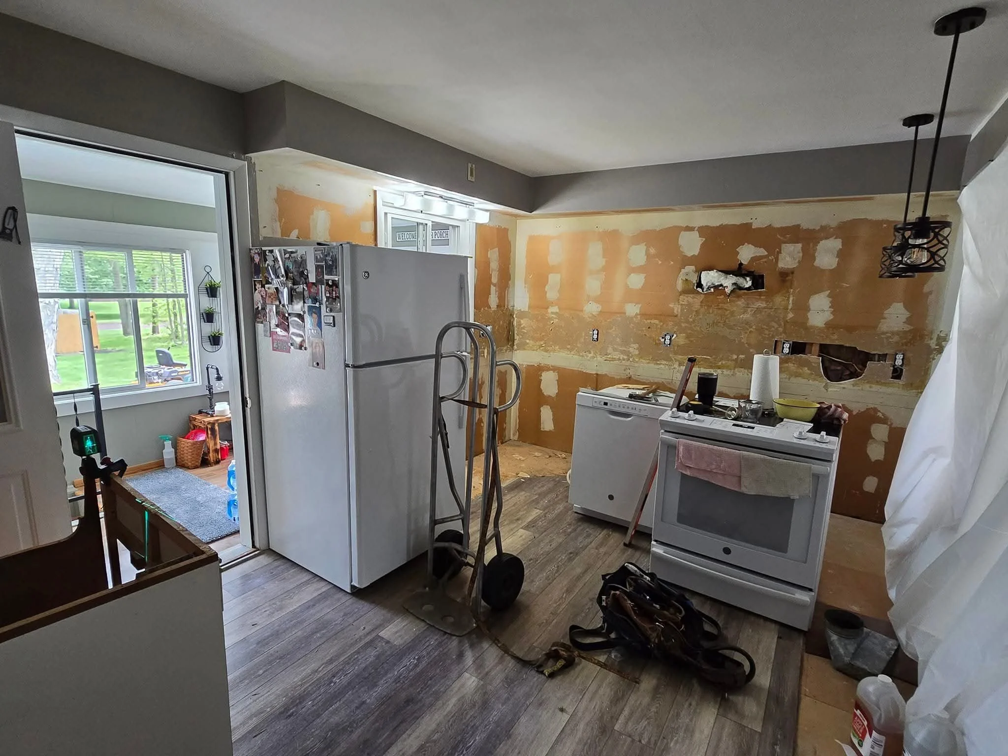 Kitchen under renovation with partially stripped wall, white refrigerator, white stove, dishwasher, and construction tools on the floor.