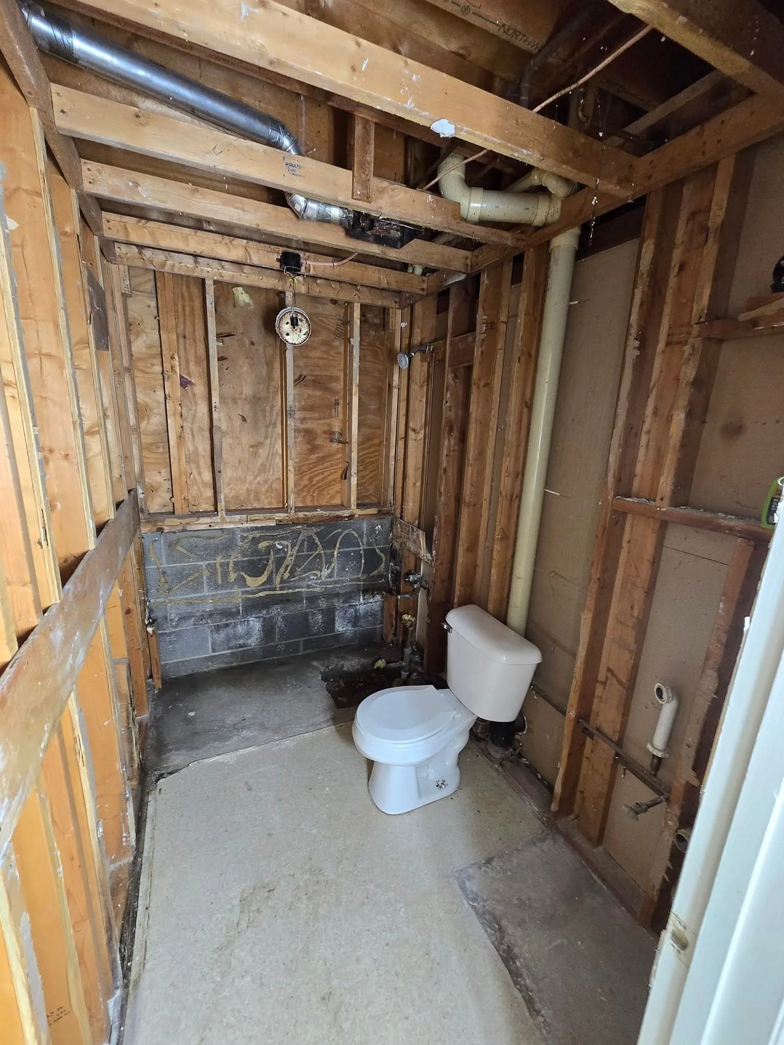 A partially renovated bathroom with exposed wooden framing, a toilet, and unfinished walls and plumbing.