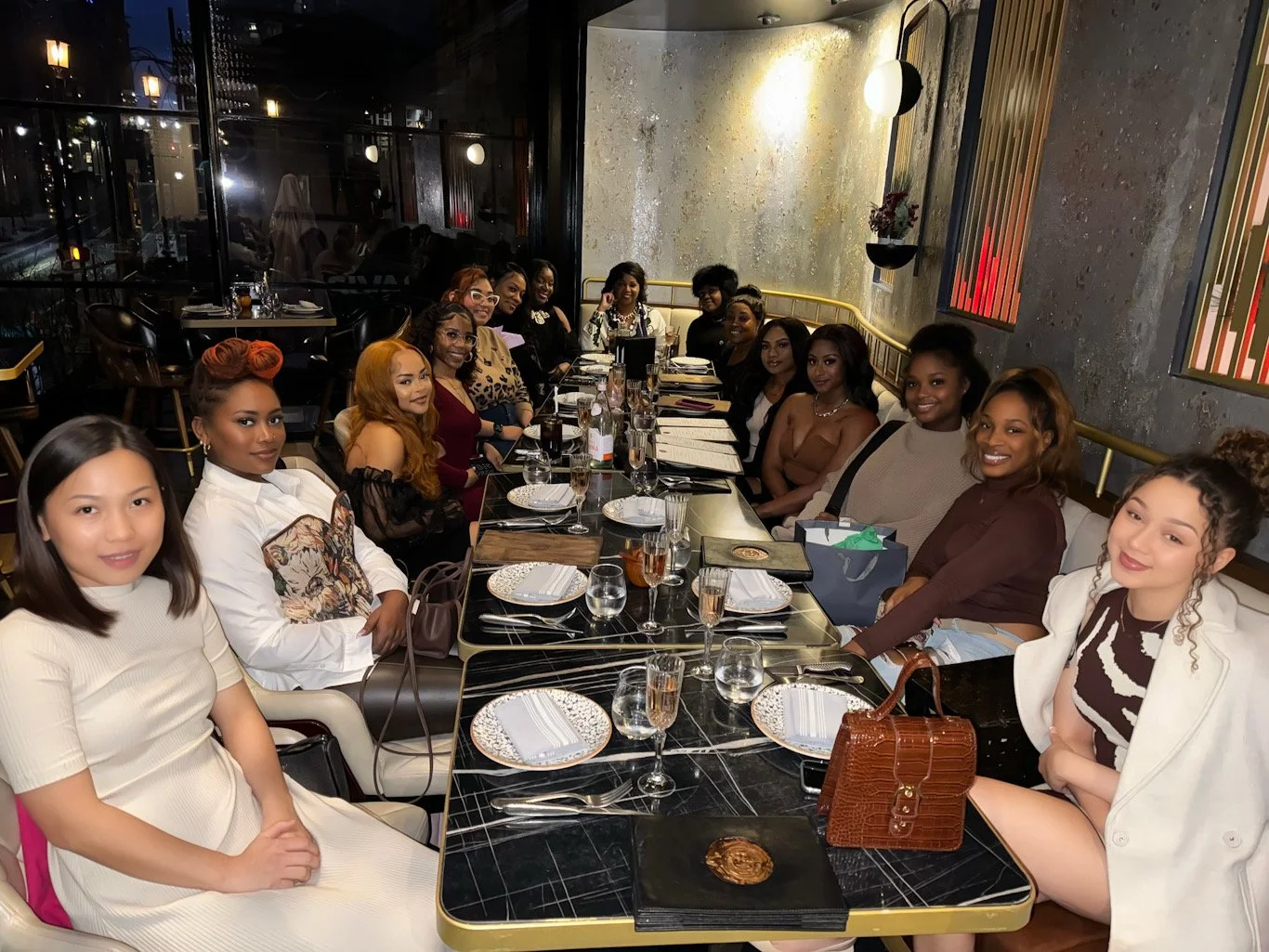 Group of women gathered around a long dining table in a restaurant setting, preparing for a meal.